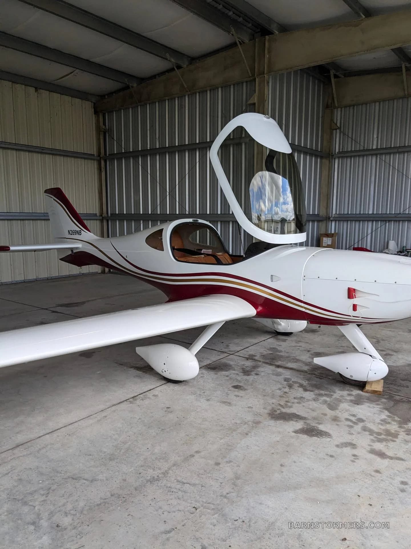 A white and red aircraft with an open canopy is parked inside a metal hangar.