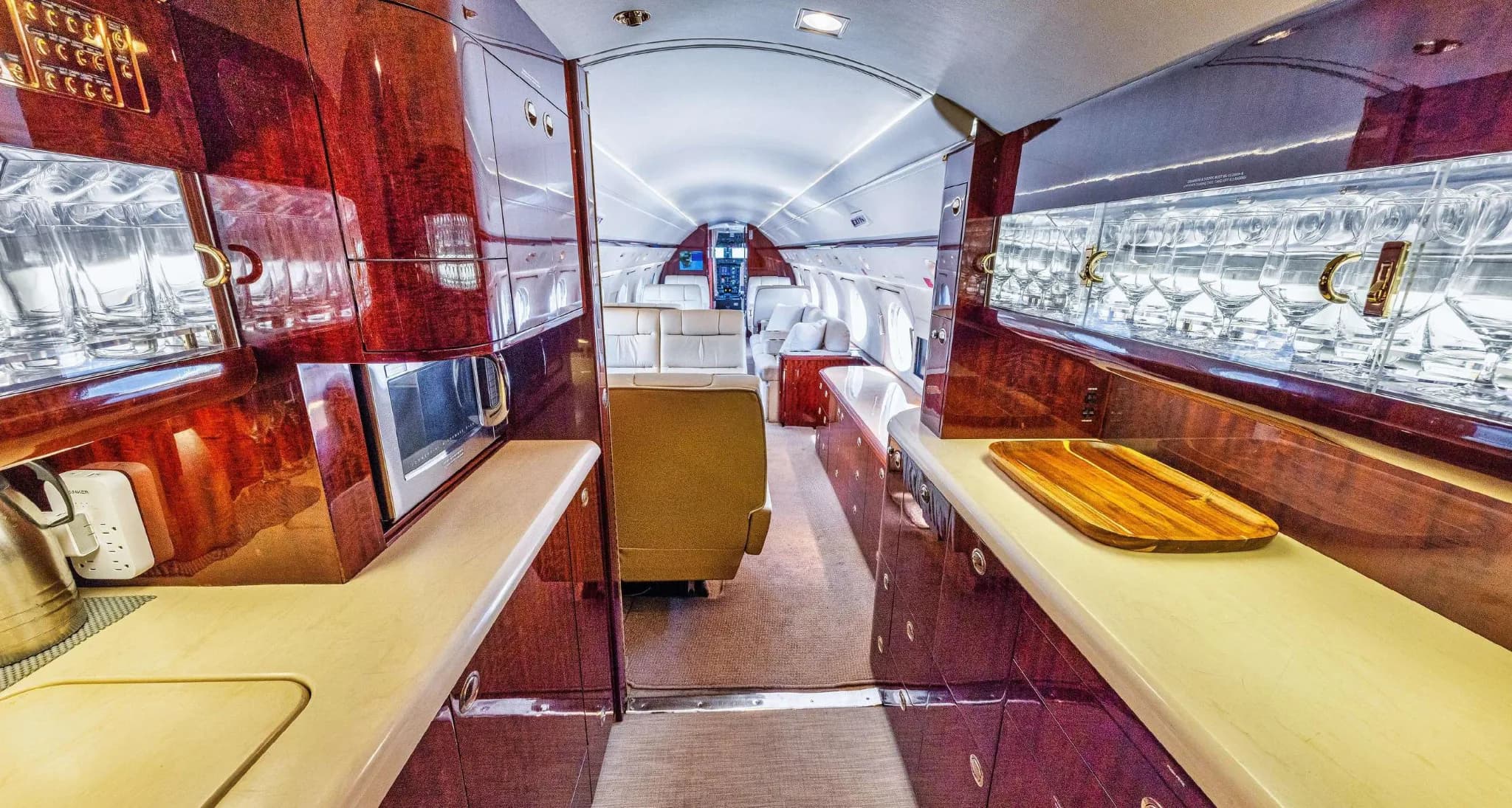 The well-equipped galley of a Gulfstream G550, featuring polished wood cabinetry and a microwave.