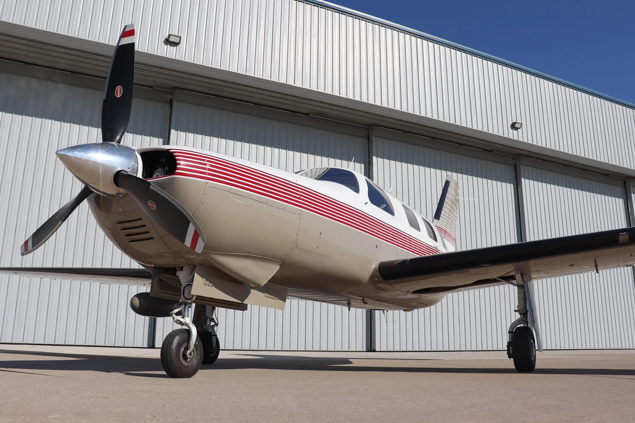 A front-quarter low-angle view of the Piper Malibu Mirage N463WB, showcasing its propeller and nose, parked by a hangar.