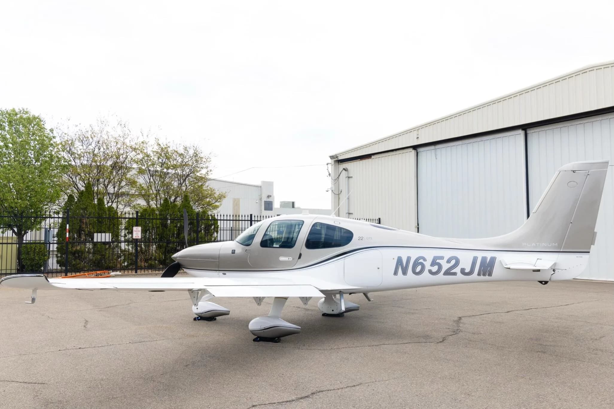 A side view of the silver and white Cirrus SR22 aircraft with N652JM registration, parked on an tarmac.