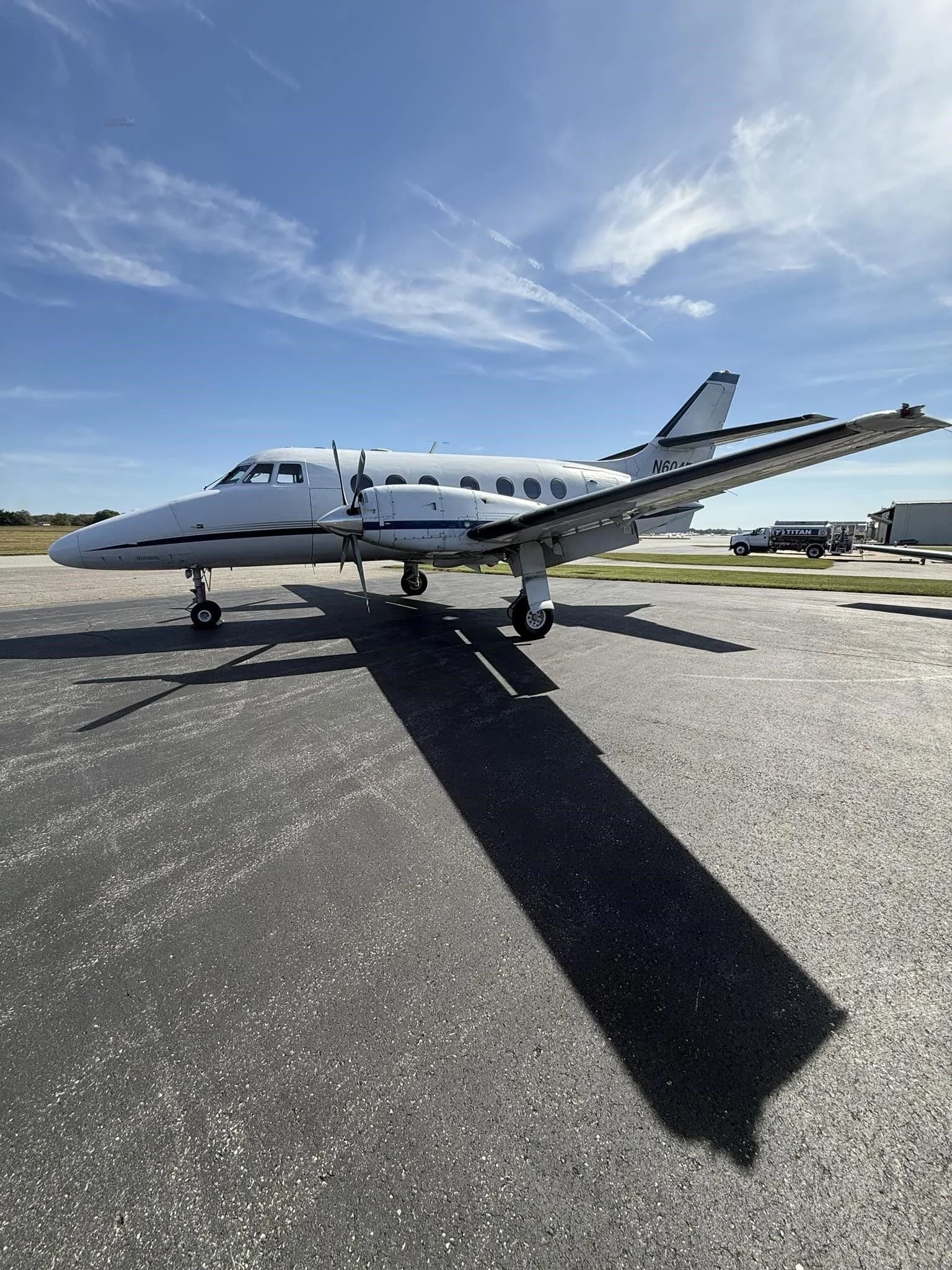A side view of a white Jetstream 31 aircraft with blue accents, tail number N604EC, parked on an asphalt tarmac under a partly cloudy sky.