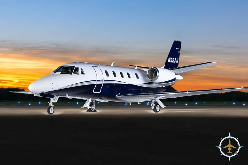 A white and blue Cessna Citation Latitude business jet with registration N327JA on a tarmac at sunset.