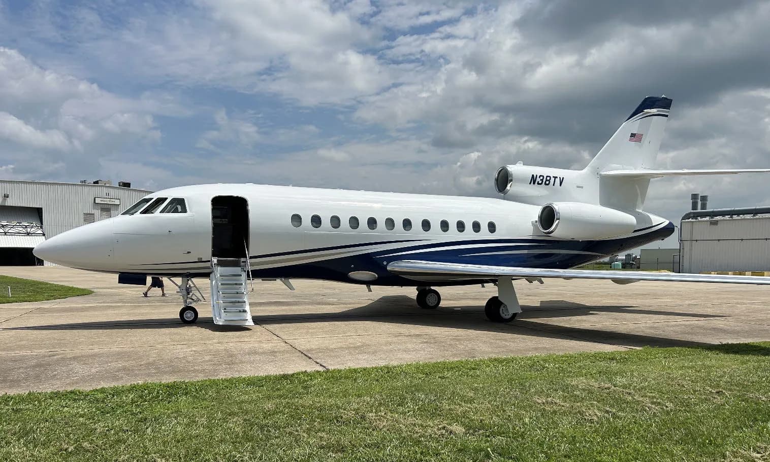 Side view of a white and blue aircraft with tail number N38TY on the tarmac with stairs extended.