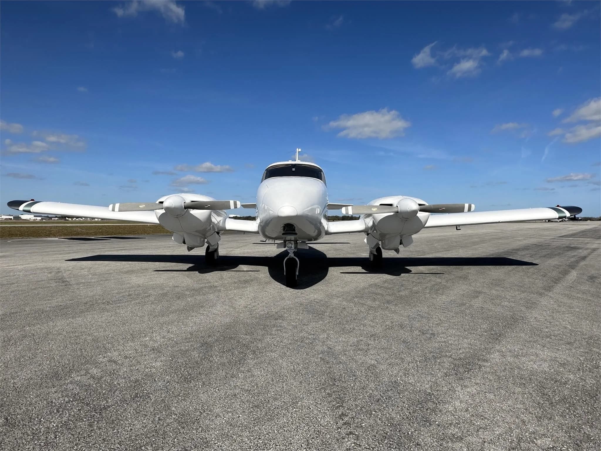 A head-on view of a white twin-engine Piper aircraft, registration N444VM, parked on an airfield.