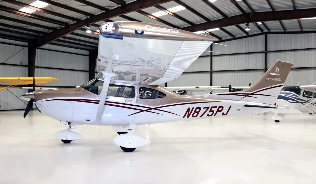 A Cessna Skylane N875PJ in a brown and white paint scheme, parked in a hangar.