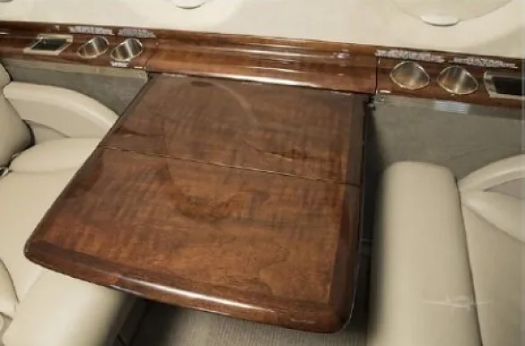A close-up of a polished wooden fold-out table in a private jet cabin, with cup holders along the side.