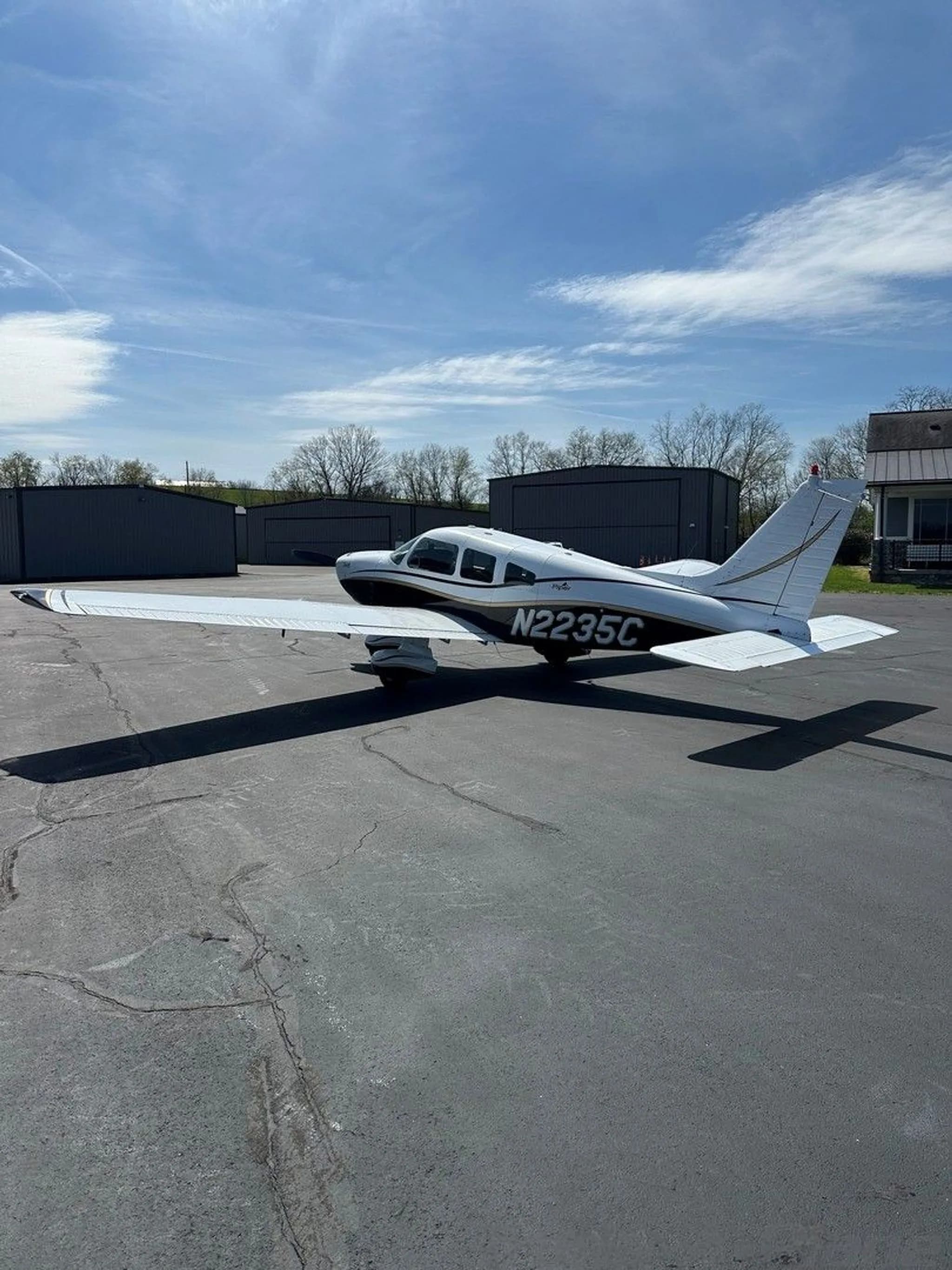 A white and black Piper aircraft with gold trim, registration N2235C, viewed from the rear-right on an asphalt ramp.