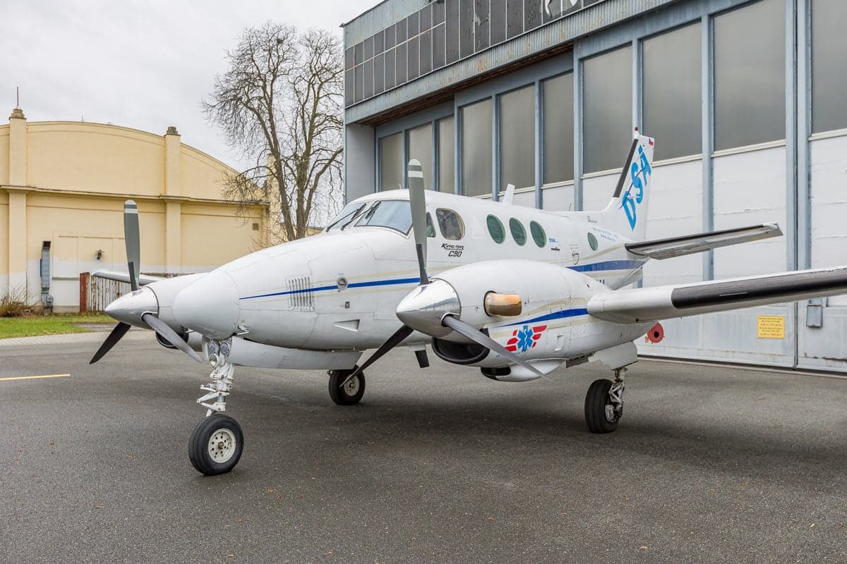 Front side view of a Beechcraft King Air C90 aircraft with a white and blue paint scheme, parked on the tarmac.