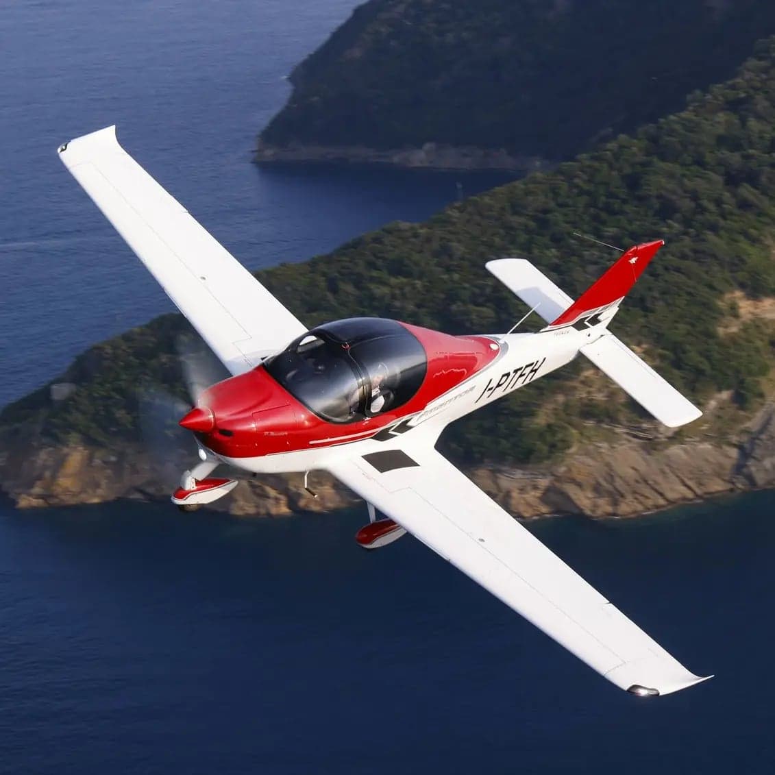 A red and white light aircraft flying over the ocean.