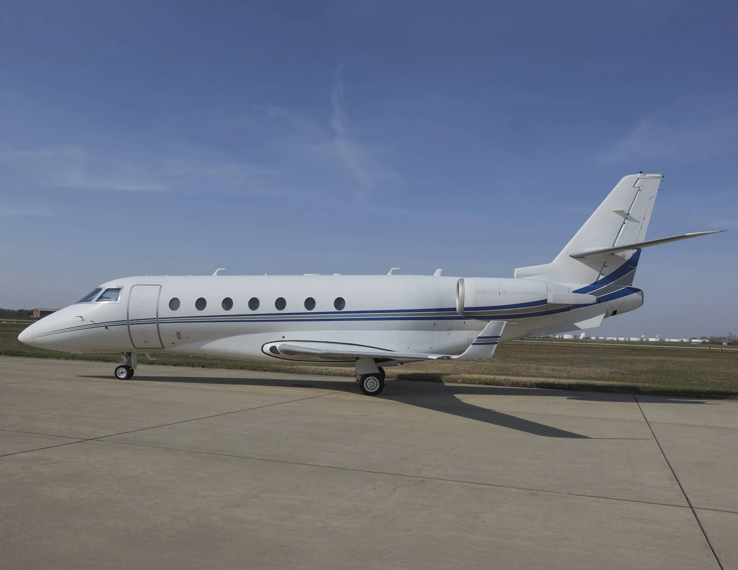 A white and blue Gulfstream jet sits on the tarmac under a blue sky.