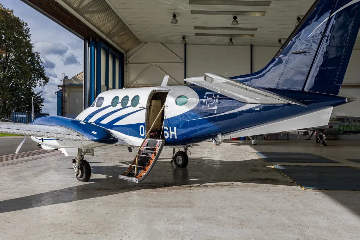A white and blue Beechcraft King Air C90 with its passenger door open and stairs extended, parked in a hangar.