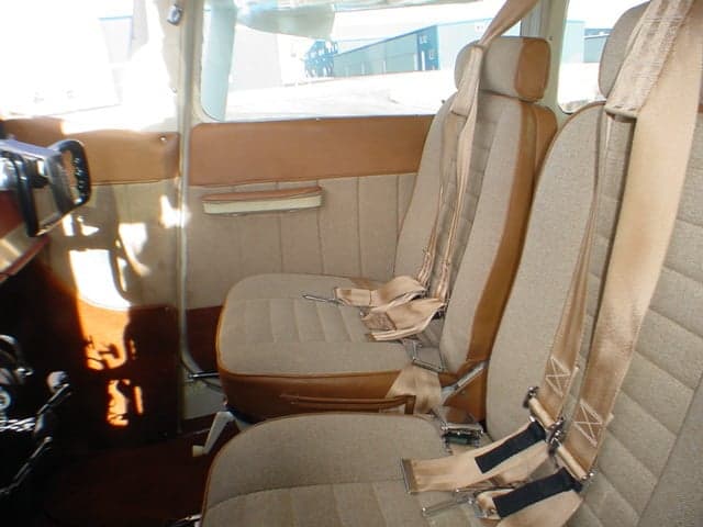The front two tan and brown fabric seats of a small aircraft cabin, with seatbelts visible.