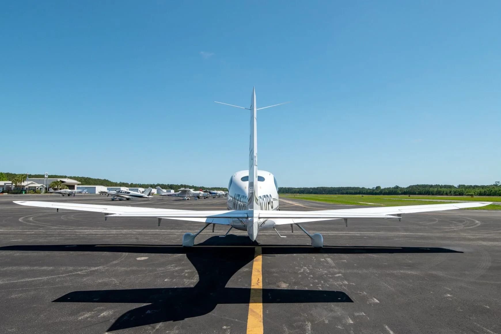 Rear view of a white Cirrus SR22T aircraft N717PG with black and grey stripes parked on an airfield.