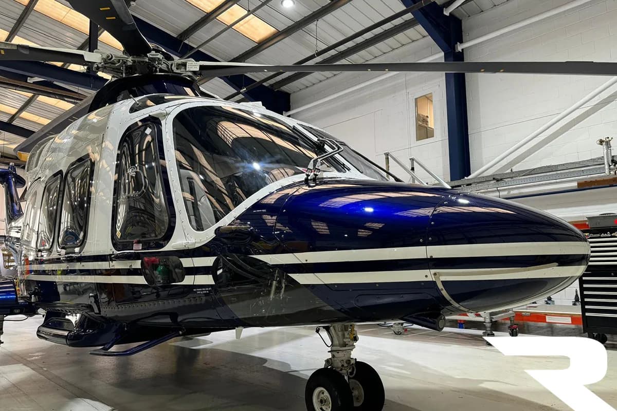 Front-right view of a blue and white helicopter with landing gear in a hangar.
