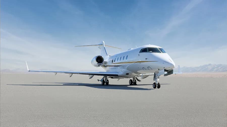 A white business jet with gold accent stripes parked on an airfield, viewed from the front-quarter.