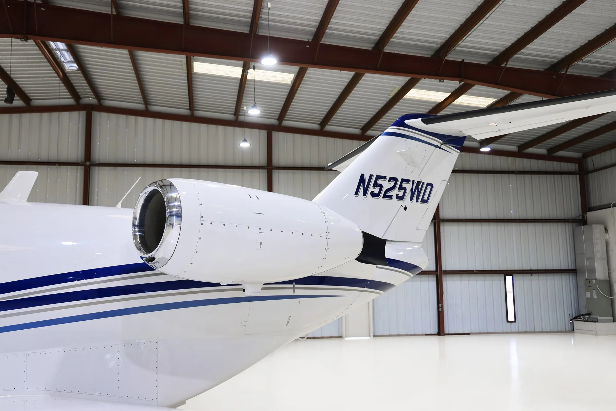A close-up of the tail and engine of a white Cessna Citation CJ2+ (N525WD) with blue stripes.