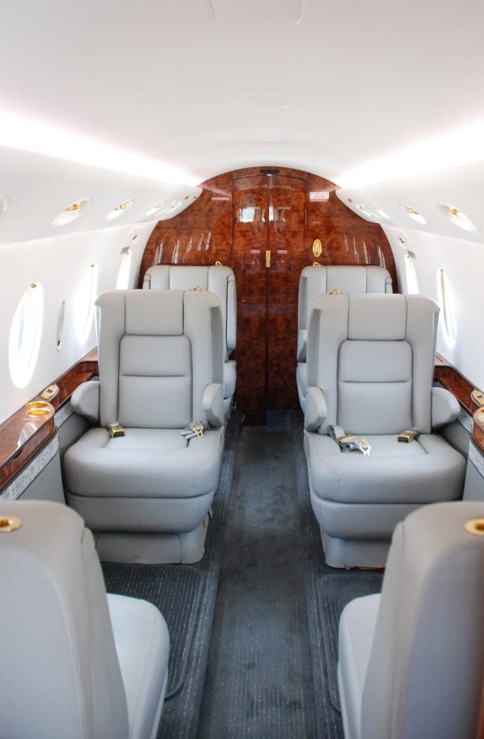 The rear section of an aircraft cabin featuring grey leather club seating and a rich wood-paneled bulkhead.