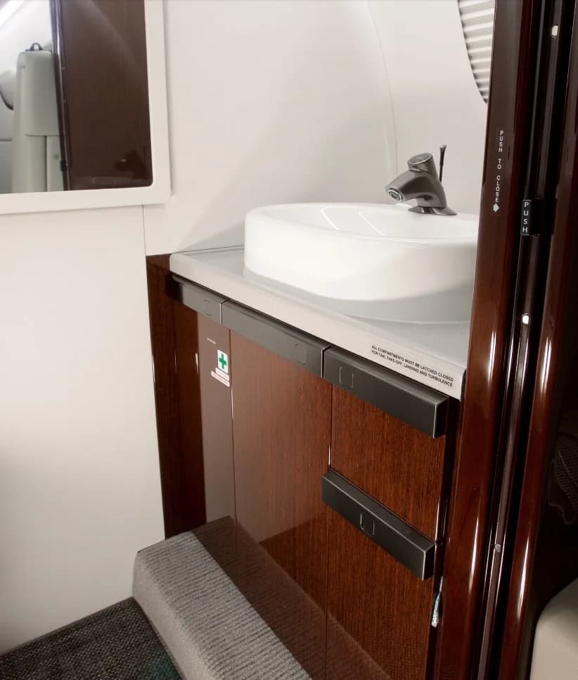A view of the aircraft lavatory, showing a white sink basin set into a dark wood vanity.