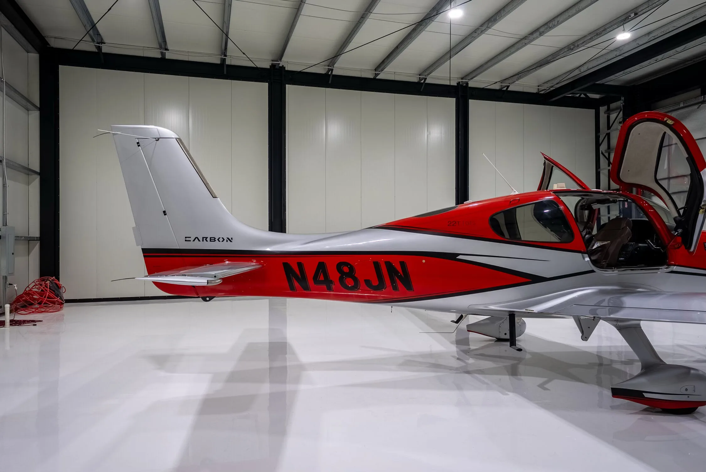 Close-up of the tail and mid-section of a red and silver Cirrus SR22T Carbon aircraft with registration N48JN and open doors.