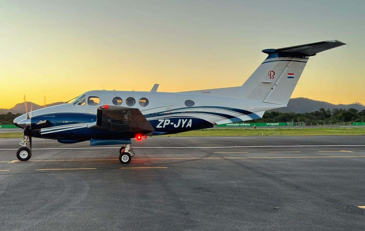 A white and blue Beechcraft King Air (ZP-JYA) turboprop aircraft on a tarmac at sunset.
