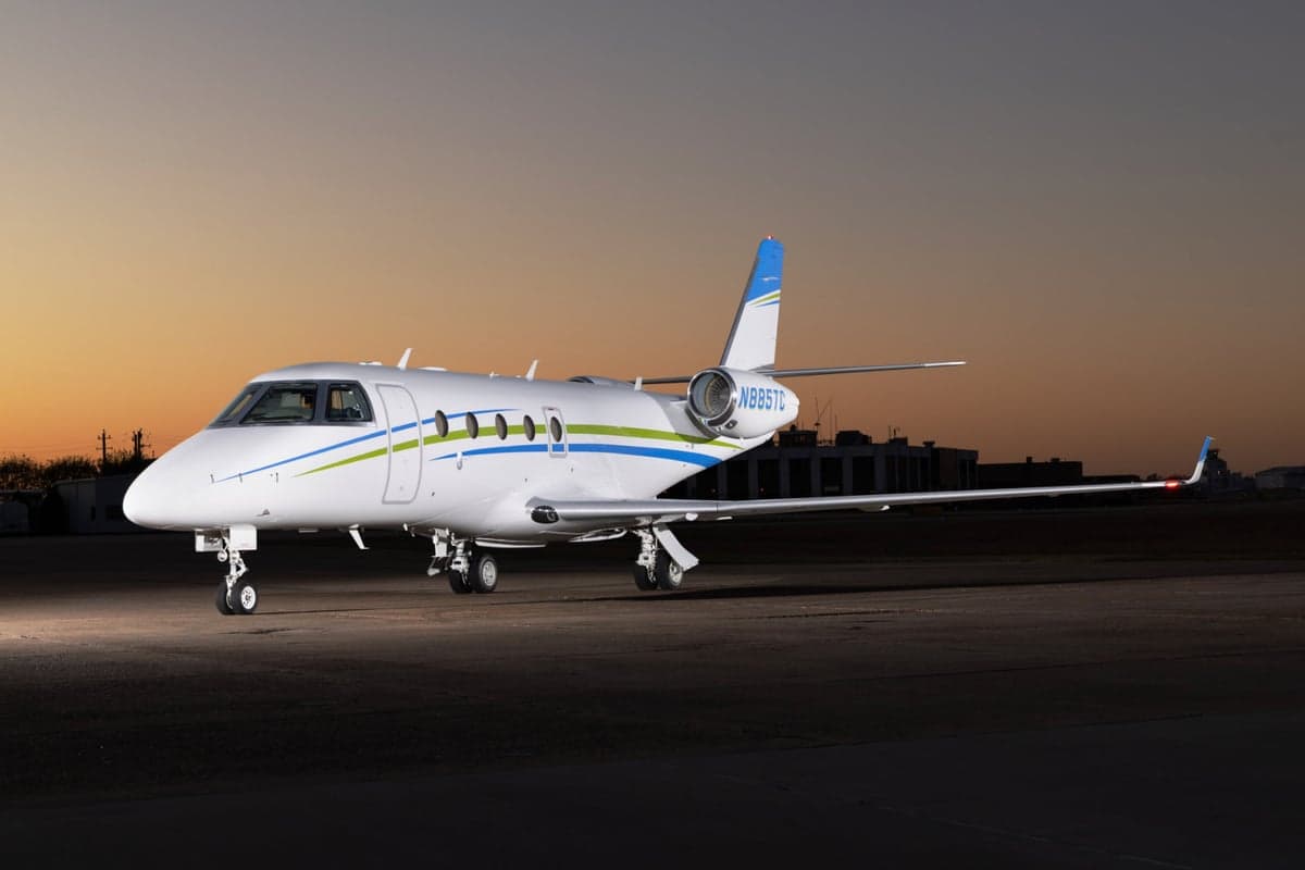 Front view of a white jet on the tarmac with a city skyline in the background.