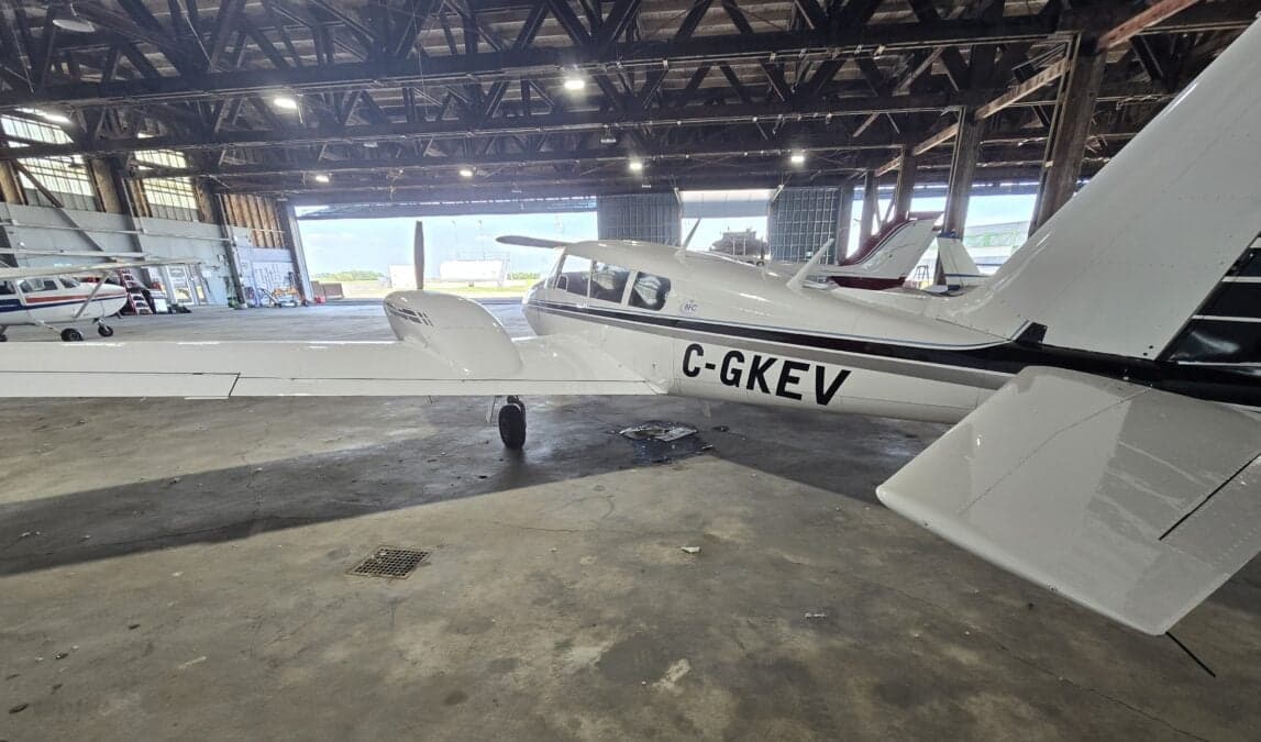 A white and black Piper PA-39 Twin Comanche is parked in a hangar.