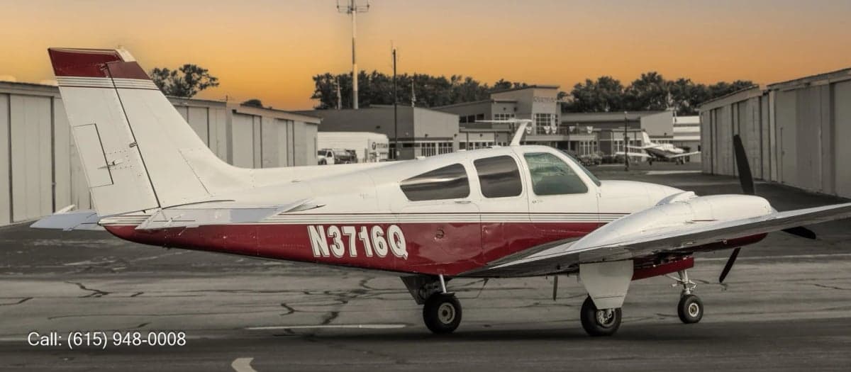 A white and red twin-engine propeller aircraft with registration N3716Q parked on an asphalt ramp at sunset, with hangars in the background.