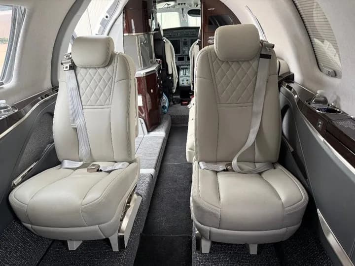 The aircraft's cabin interior with light-colored quilted leather seats, looking towards the cockpit.