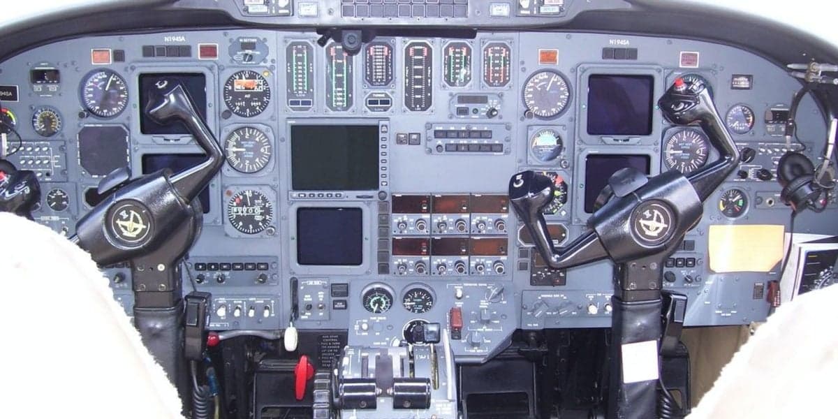 The cockpit of a Cessna Citation jet, showing the instrument panel with multiple screens and controls, and two yokes.