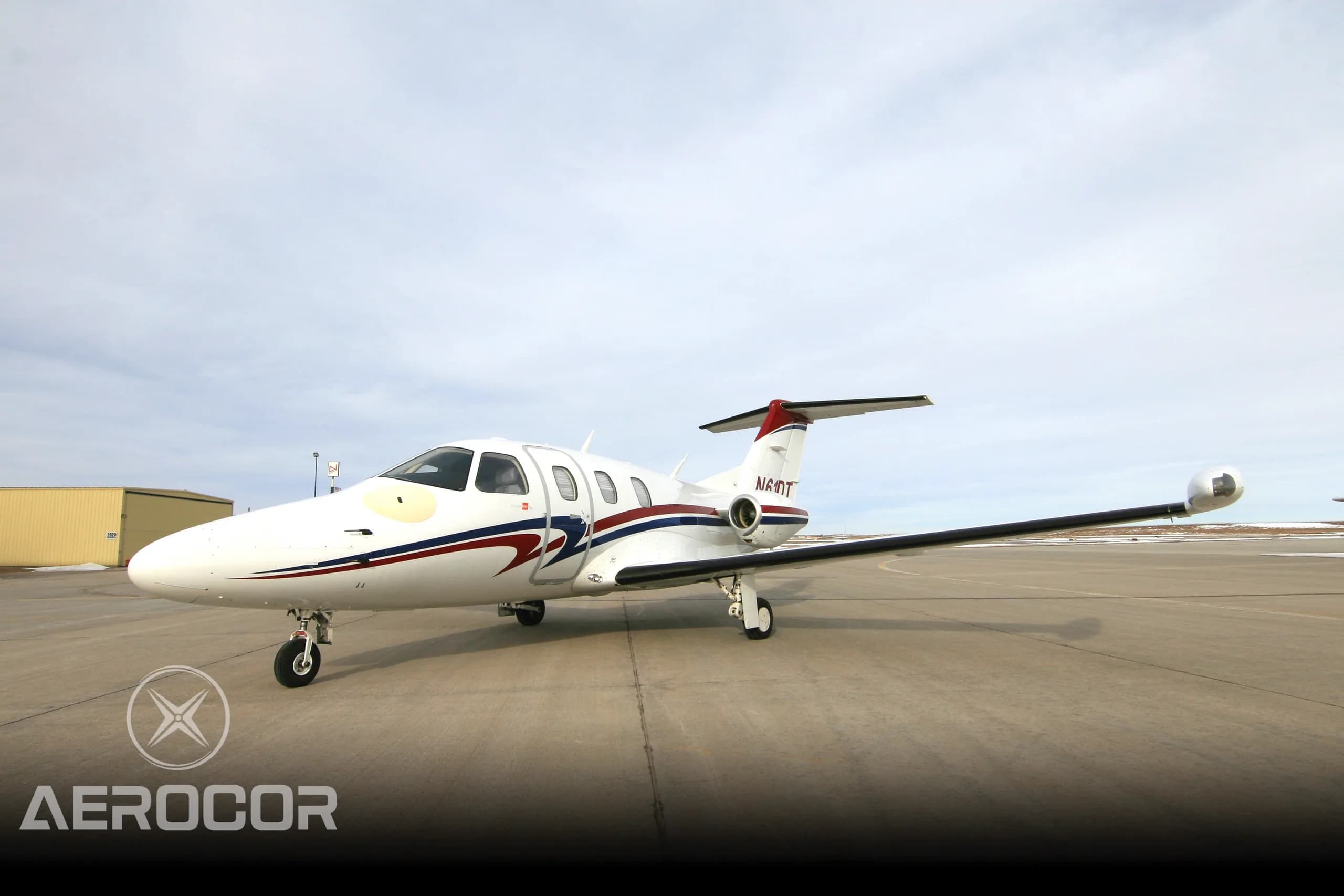 A white Eclipse 500 jet with red and blue stripes parked on an airport tarmac.