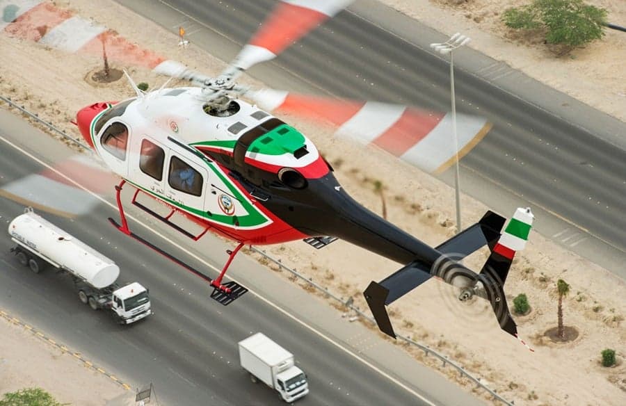 A helicopter with red, white, and green stripes flies over a highway.
