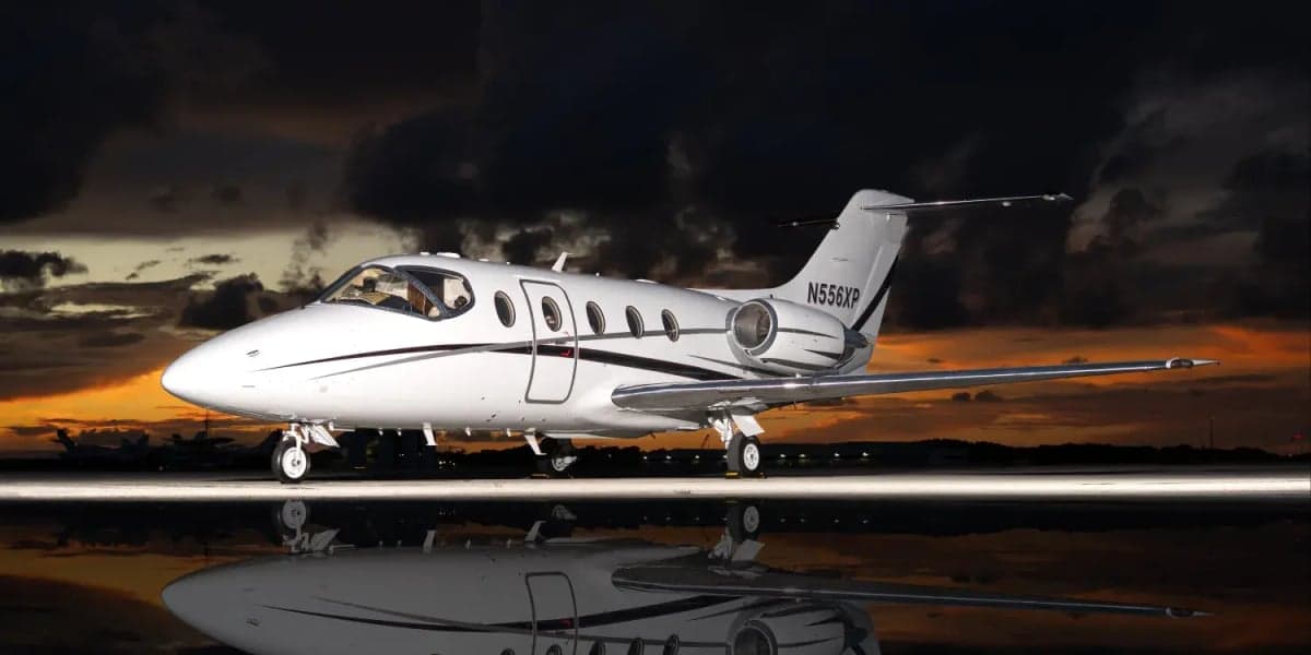 A white Learjet is reflected on the tarmac at sunset.