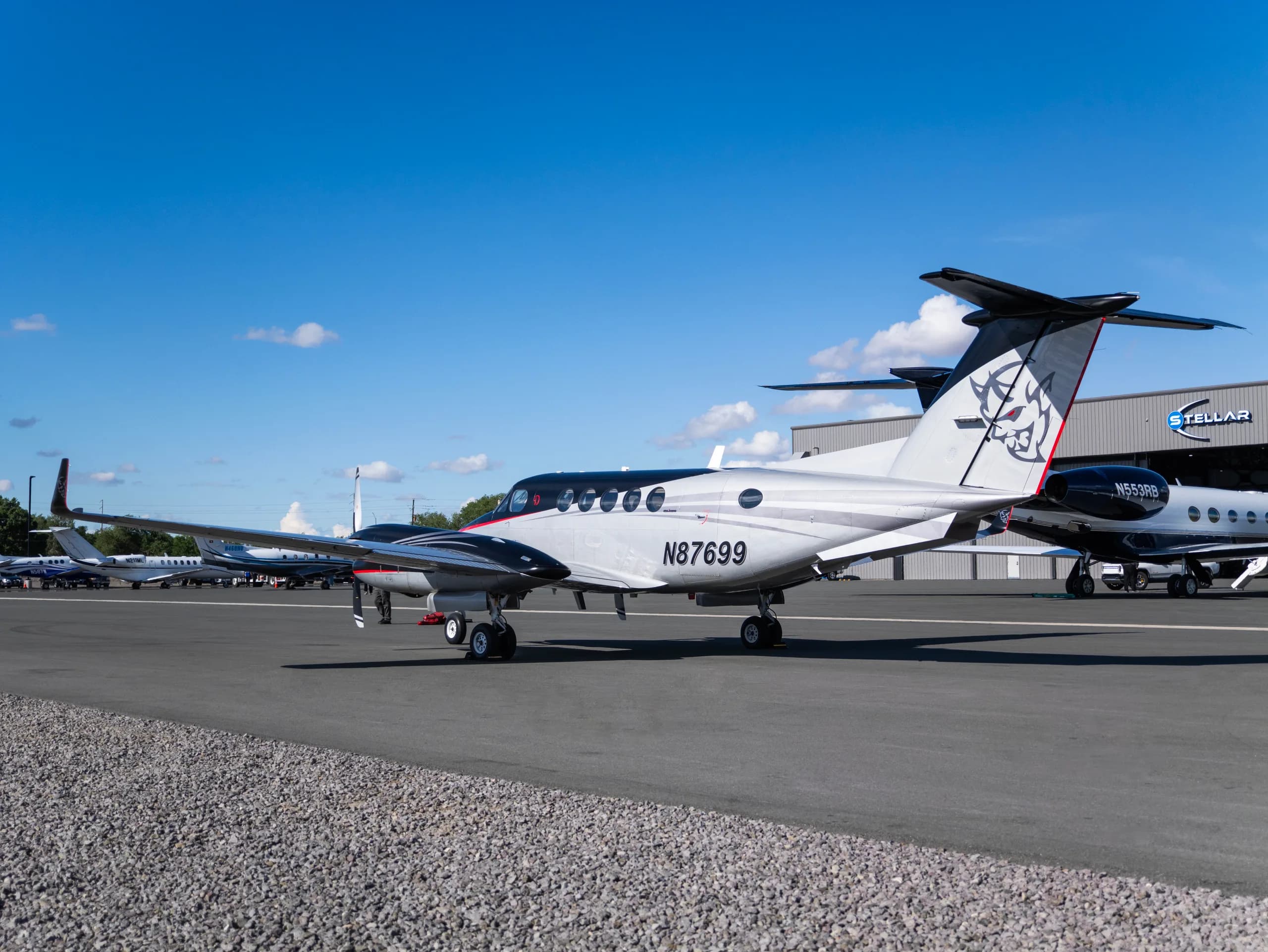 The N87699 twin-turboprop aircraft, painted silver and black with red accents and a custom tail logo, parked on an airport tarmac.