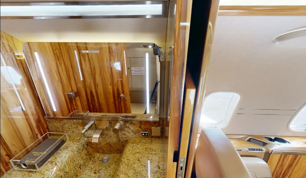 The lavatory sink area of a private jet, featuring a granite countertop, mirror, and polished wood paneling.