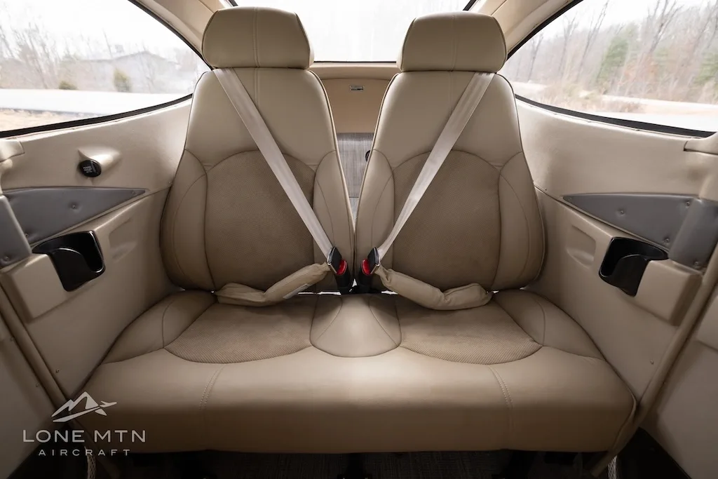 The light tan leather interior of an aircraft cabin, showing the rear bench seat and two front seats.