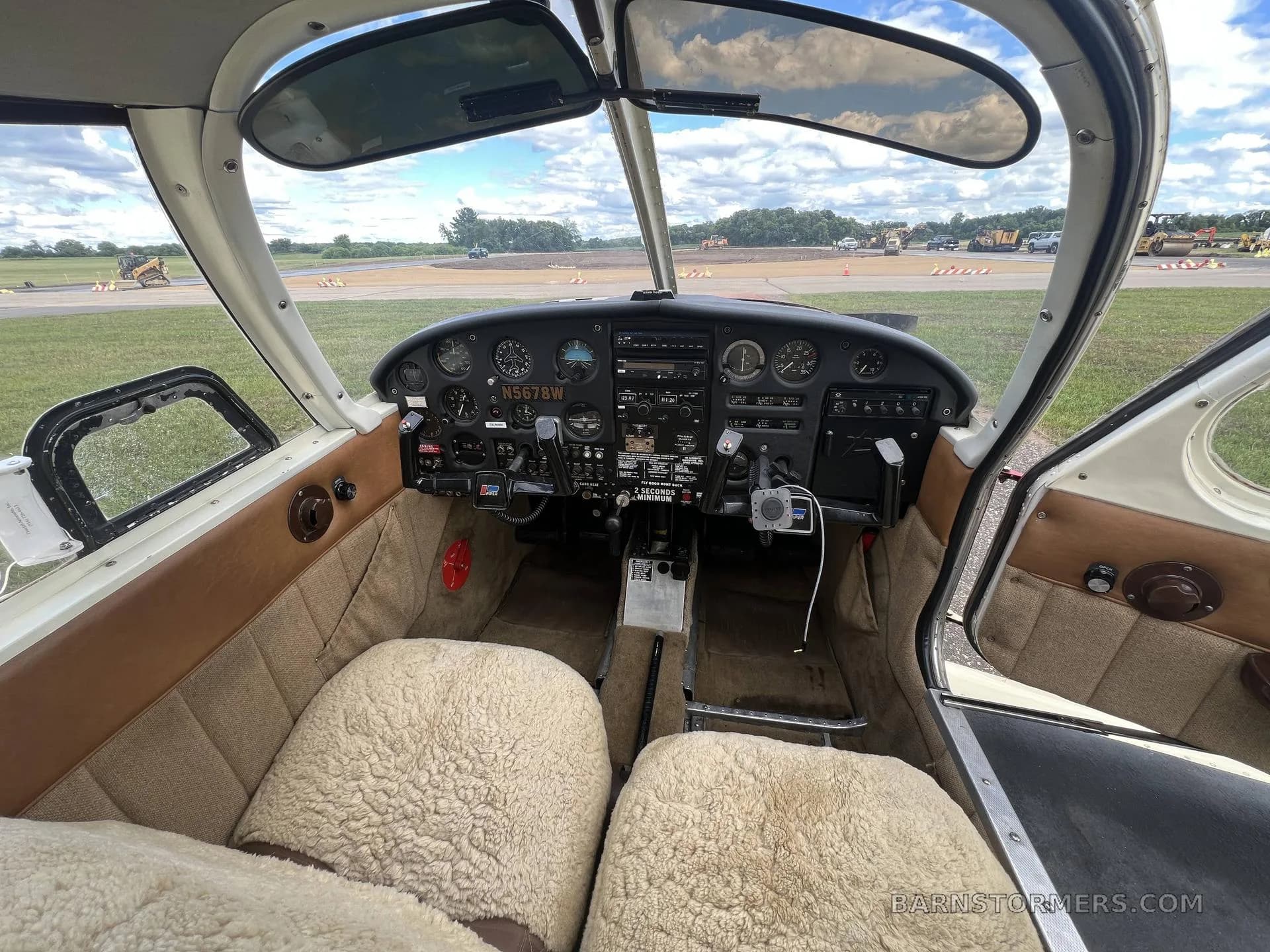 The cockpit of a single-engine aircraft showing the instrument panel, controls, and sheepskin-covered seats.