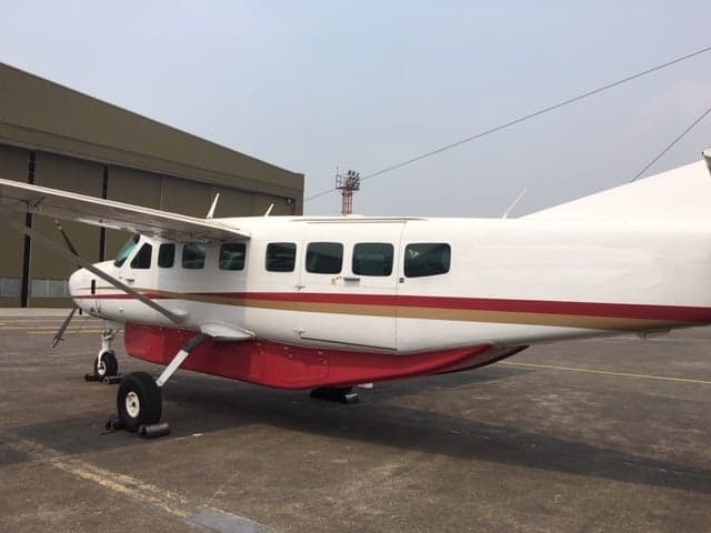 A white and red Cessna Caravan aircraft parked on an airfield, viewed from the side.