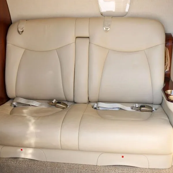 A light beige leather two-person bench seat with seatbelts in a private jet cabin.