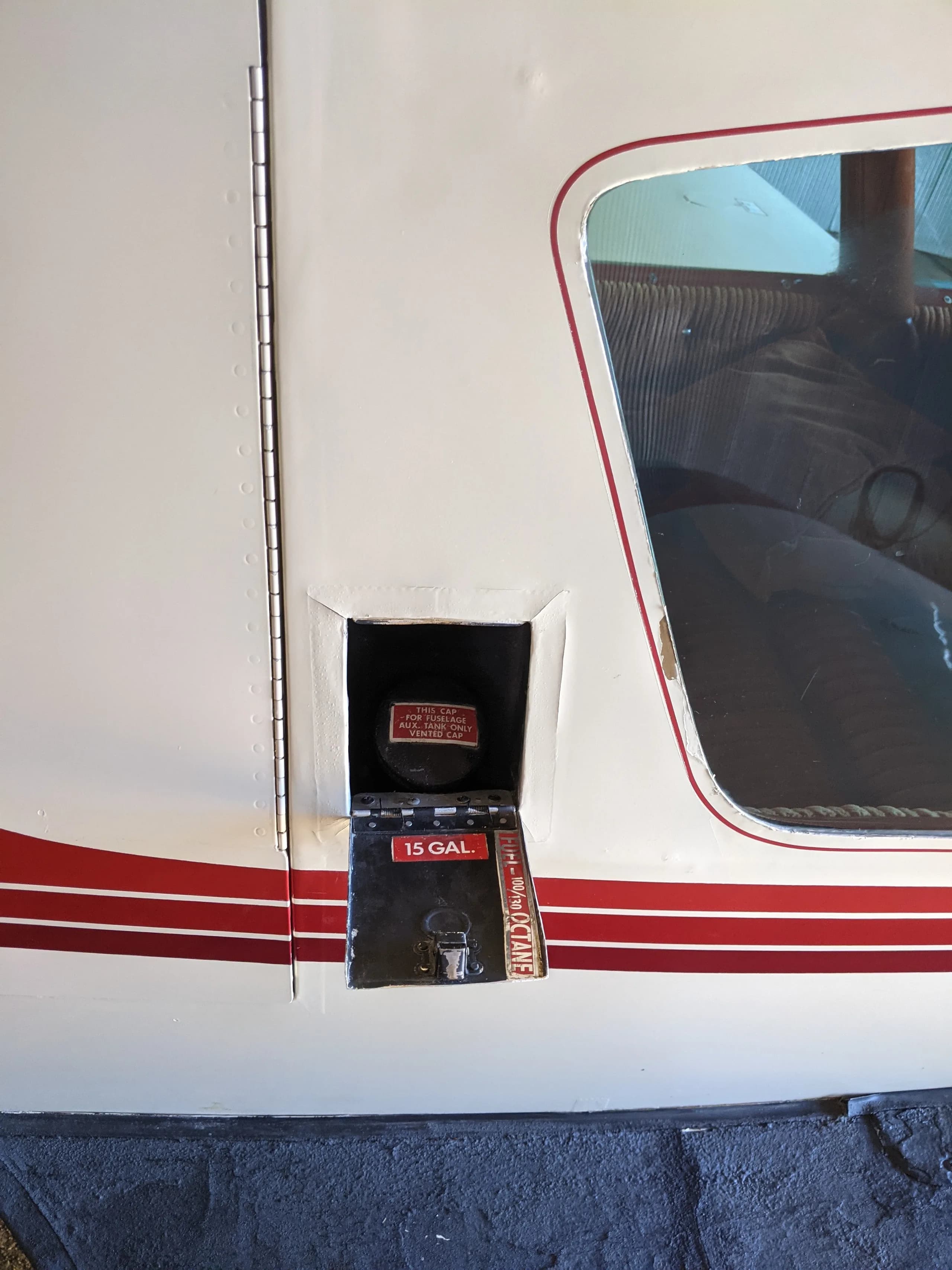 A close-up of a 15-gallon auxiliary fuel access panel on the white and red fuselage of the aircraft.