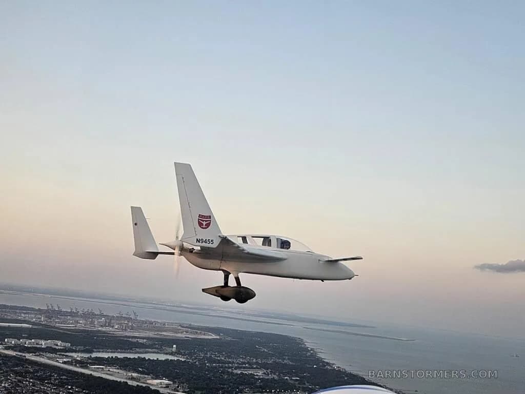 A white Rutan Long-EZ aircraft with registration N9455 flying over a coastal area at sunset.