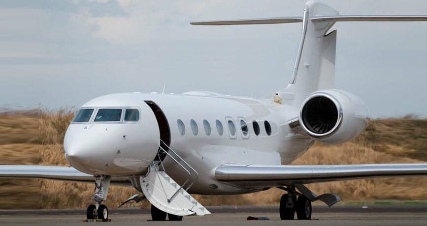 A white private jet is parked on the tarmac with its door open.