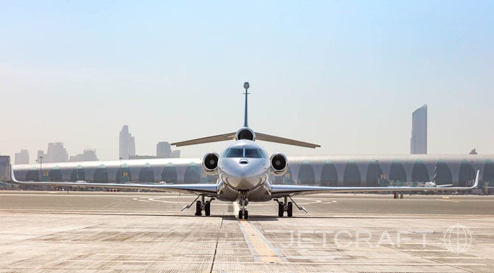 Front view of a Falcon aircraft on the tarmac with a city skyline in the background.