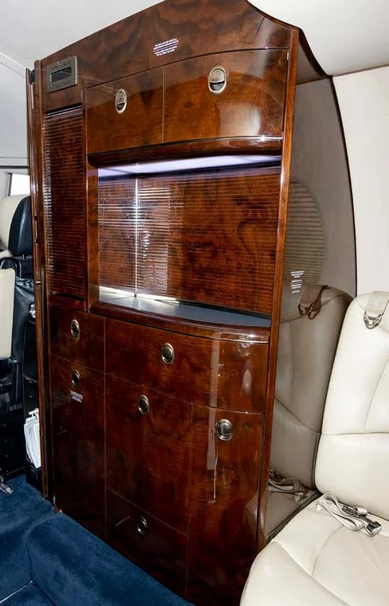 A tall, dark wood cabinet with multiple drawers and compartments inside a business jet's cabin.