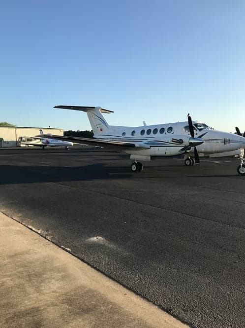 A King Air parked on the tarmac with other aircraft in the background.