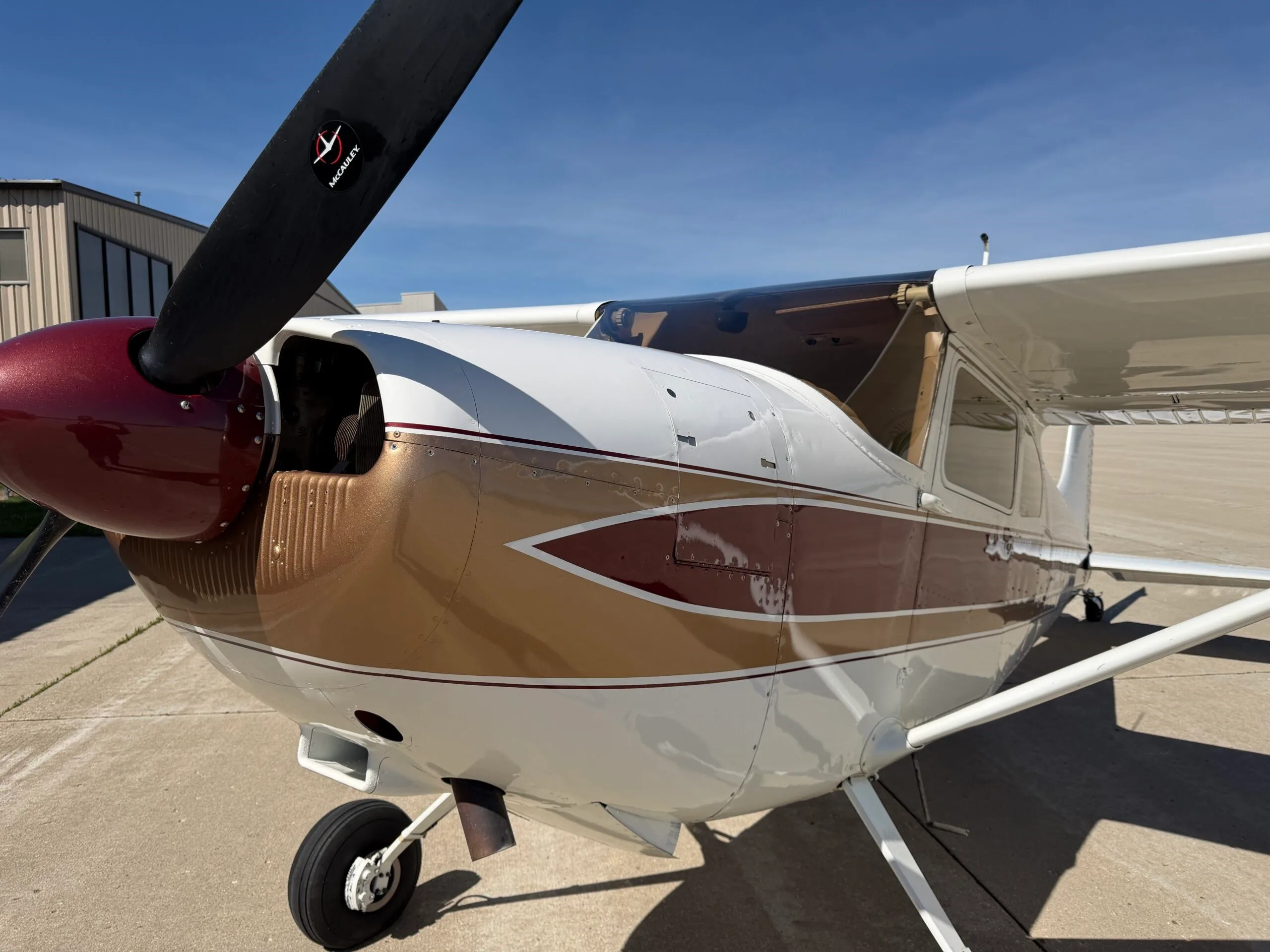 Front-left view of the fuselage and propeller of a white, gold, and maroon Cessna 172.