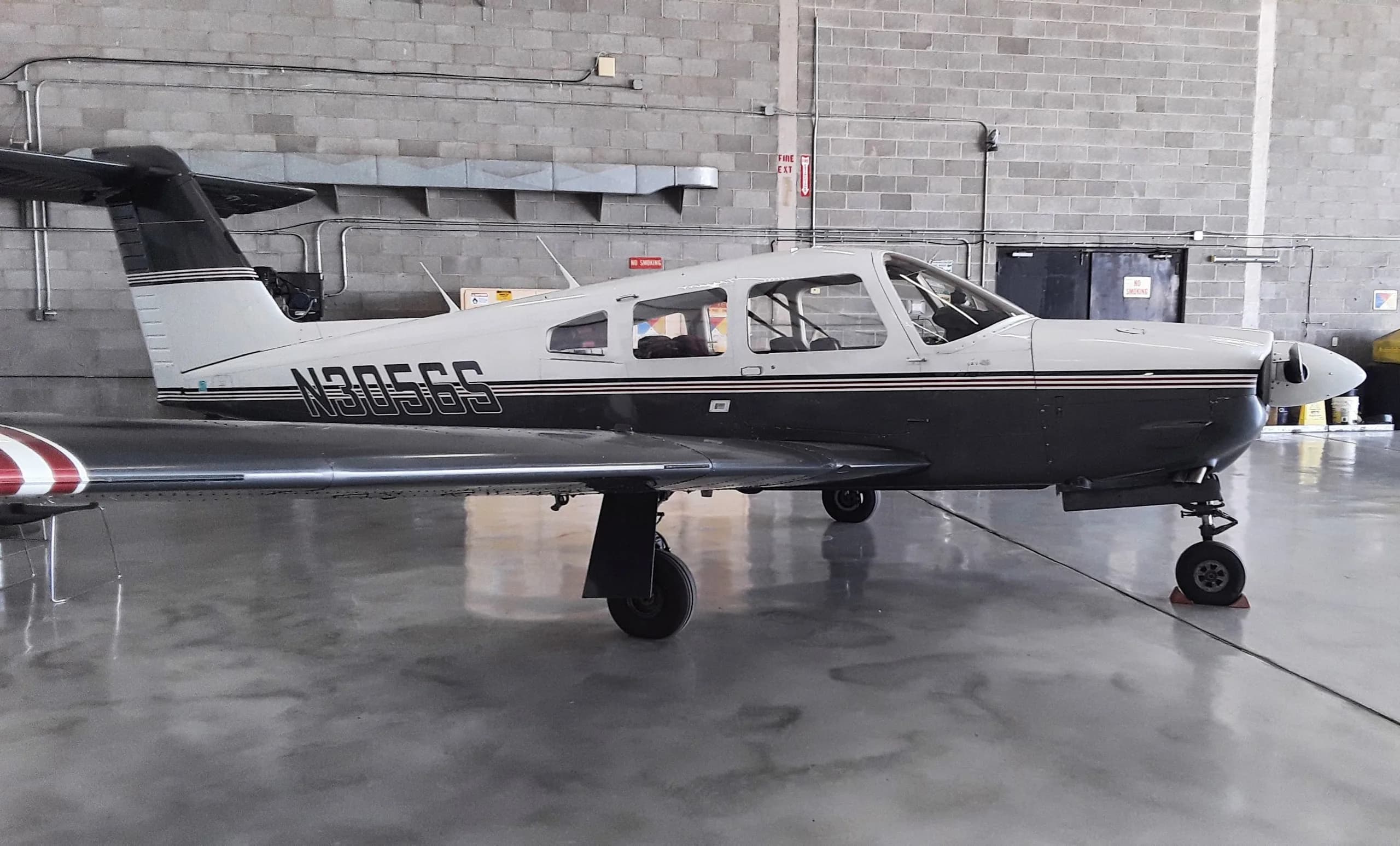 A white and dark grey single-engine propeller aircraft with registration N305GS parked in a hangar.