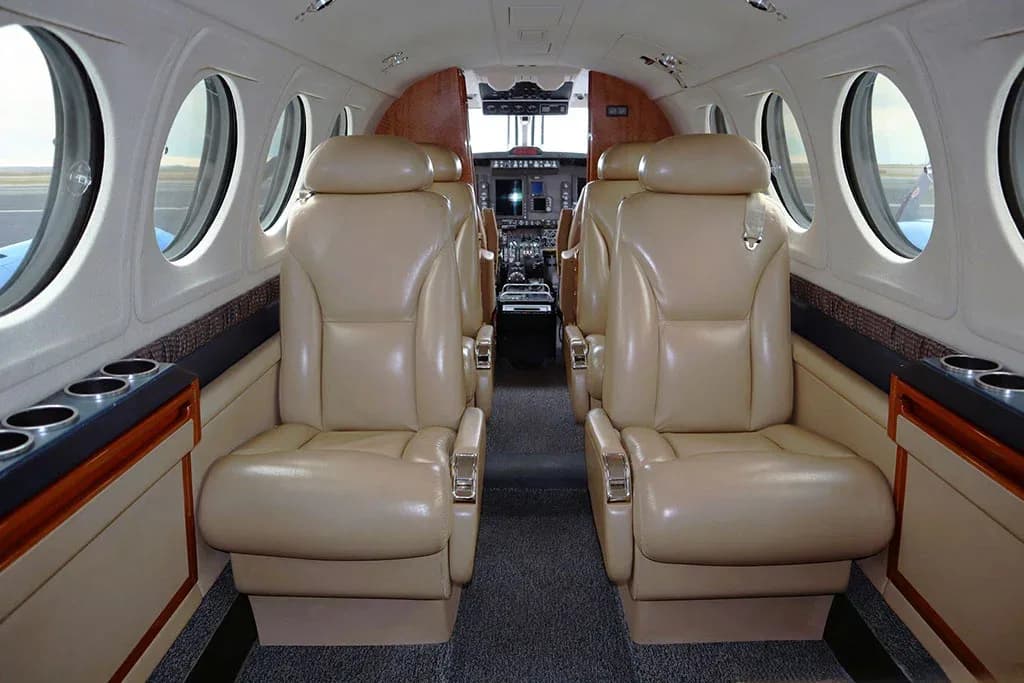 The interior cabin of an aircraft with tan leather seats arranged in a club configuration, facing the cockpit.