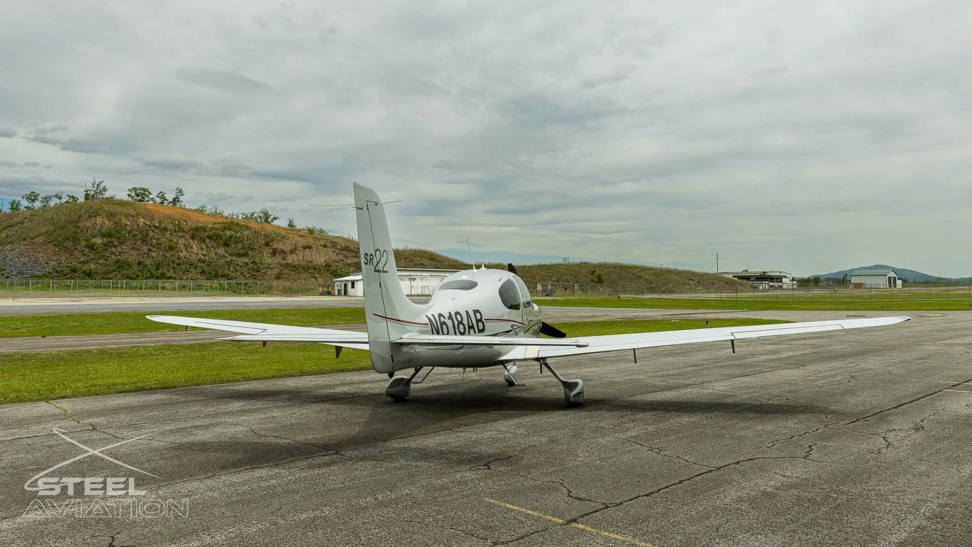 A silver Cirrus SR22 GTS aircraft with registration N618AB parked on an tarmac, viewed from the rear.