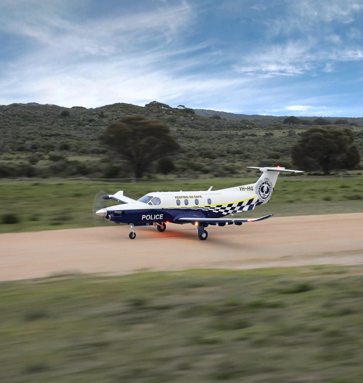 A Pilatus PC-12 aircraft with police livery taxis on a dirt runway.