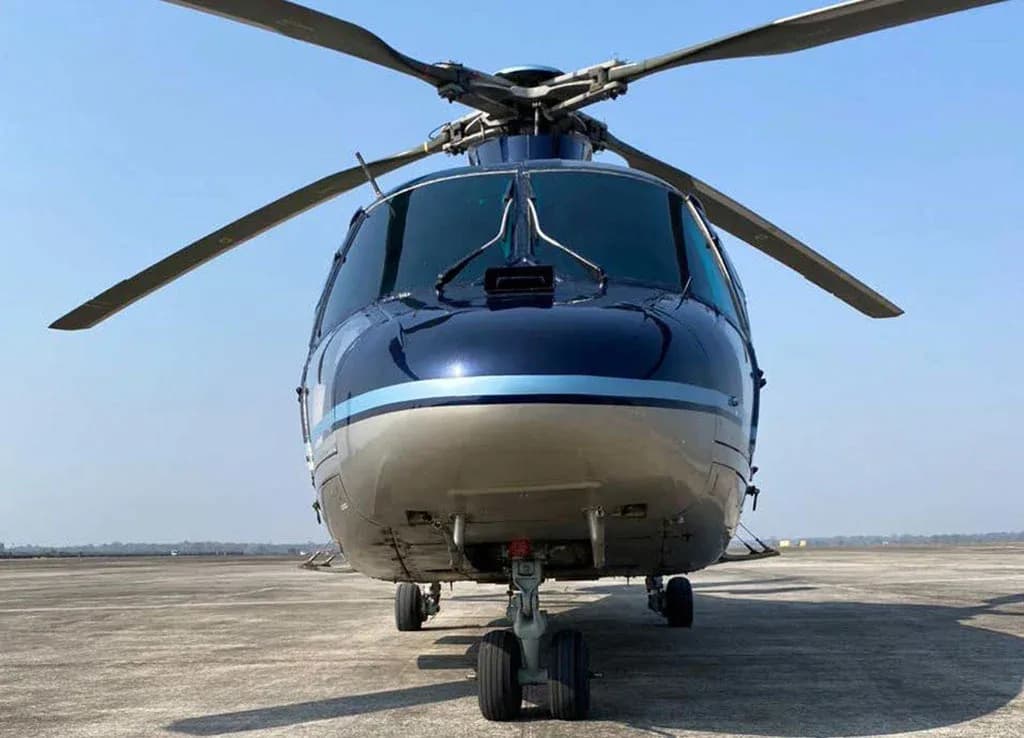 A head-on view of a dark blue and silver Airbus H155 helicopter parked on an airfield.